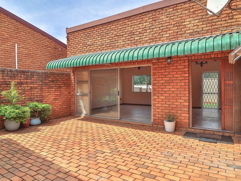 A private paved courtyard area featuring facebrick walls, a metal awning, and direct access to the interior living space through a sliding door.