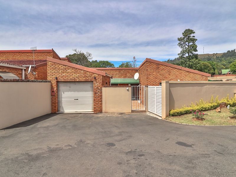 Front exterior view of a brick townhouse featuring a single roller garage door, secure gated entrance, and paved driveway area.