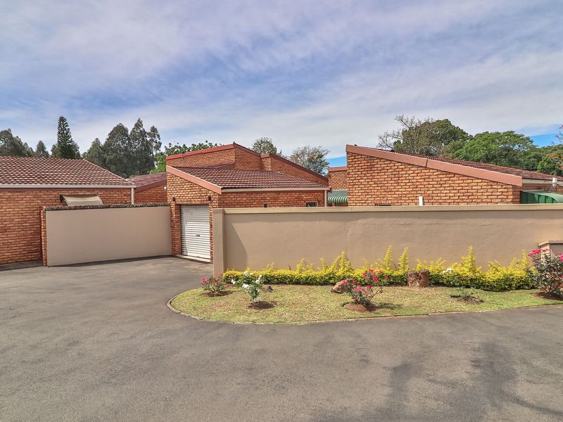 Front exterior view of a townhouse complex featuring face-brick construction, tiled roofing, a private garage, and a well-maintained boundary wall with landscaped garden beds.