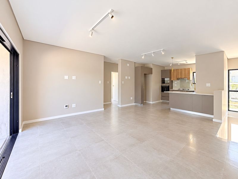 Spacious open-plan living and kitchen area featuring modern neutral finishes, tiled floors, track lighting, and a well-appointed kitchen with built-in appliances.