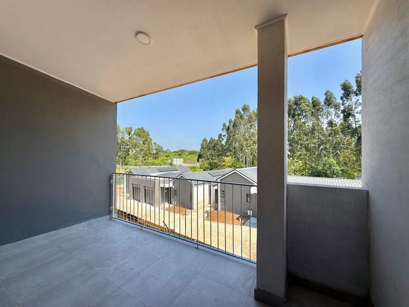 A clean, modern covered balcony featuring tiled flooring, a metal balustrade, and a structural support column, offering an open view of the surrounding area.