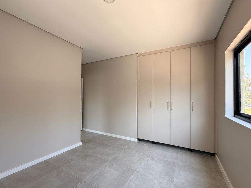A bright, empty bedroom featuring neutral wall tones, modern tiled flooring, and ample built-in cupboard storage.