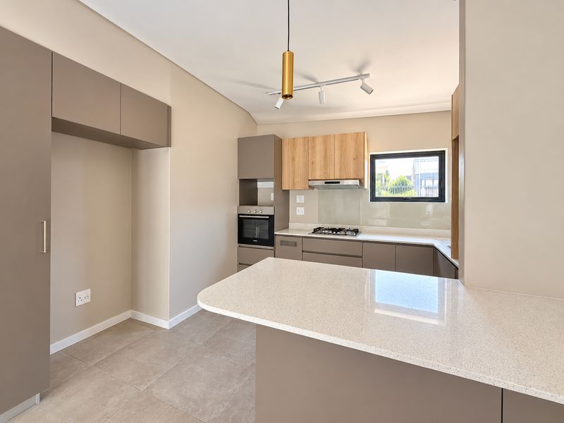 Modern kitchen featuring sleek built-in cabinetry, stone countertops, integrated oven, gas hob, and contemporary lighting fixtures in a clean, neutral space.