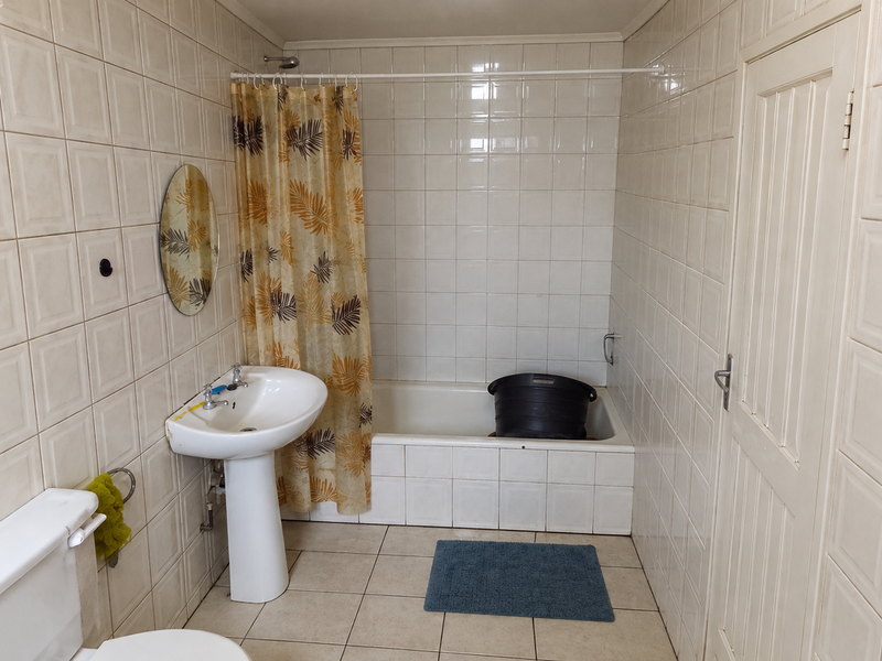 A functional bathroom featuring a pedestal basin, bathtub with shower curtain, and full-height wall tiling. The space offers a classic, dated layout.