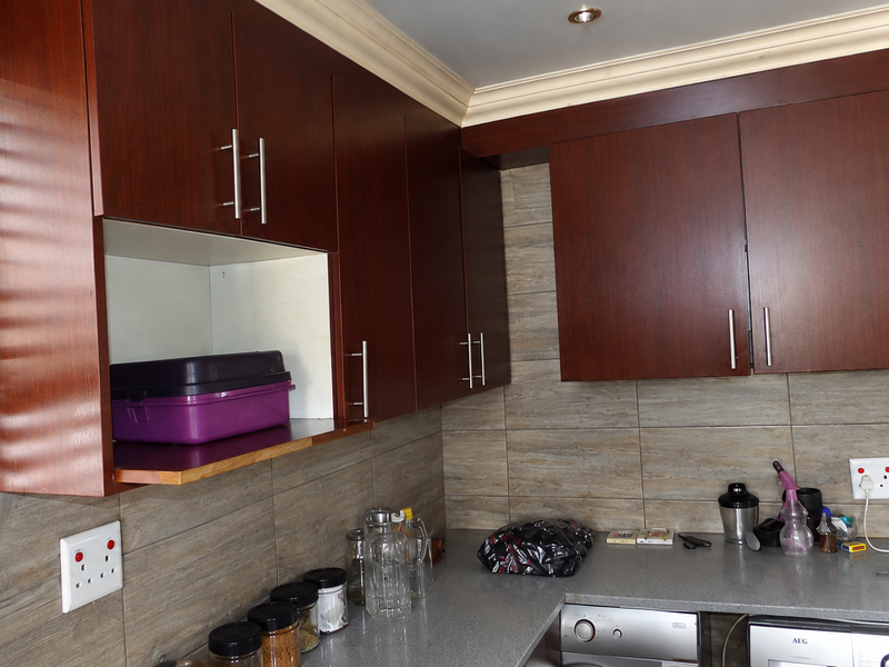 A functional kitchen area featuring dark wood cabinetry, stone countertops, and tiled backsplash with integrated laundry appliances.