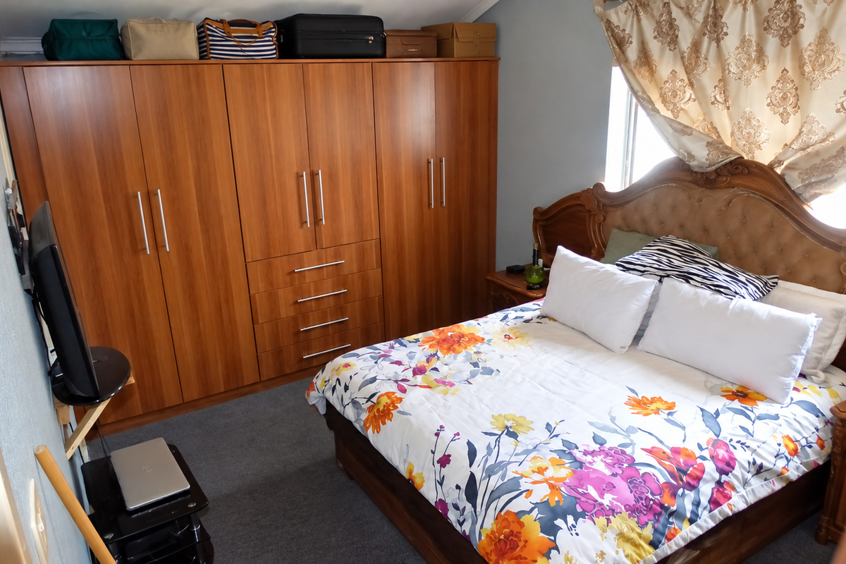 A bedroom featuring a large built-in wooden wardrobe and carpeted flooring, providing ample storage space.