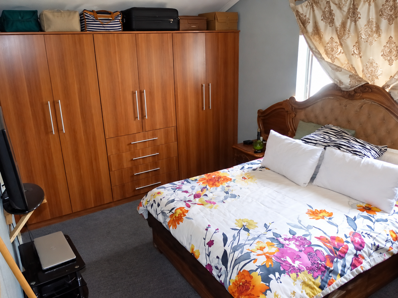 A bedroom featuring a large built-in wooden wardrobe and carpeted flooring, providing ample storage space.
