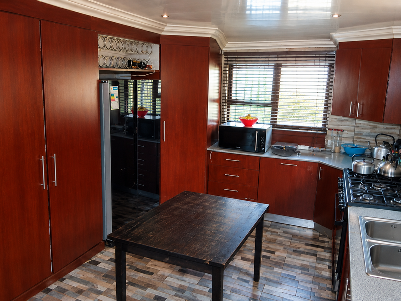 A functional kitchen featuring dark wood cabinetry, a gas hob, double stainless steel sink, and tiled splashbacks with natural light from venetian blinds.