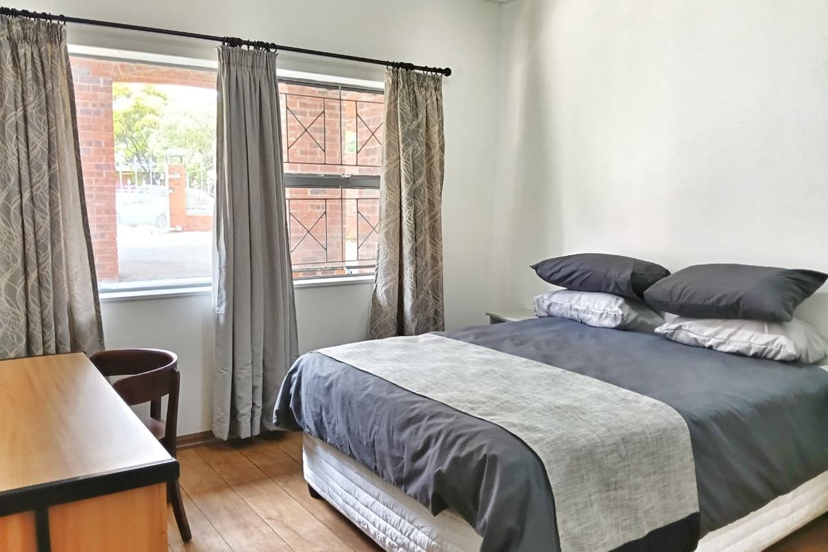 A bedroom featuring wooden flooring and a window with security bars, providing a functional and well-lit living space.