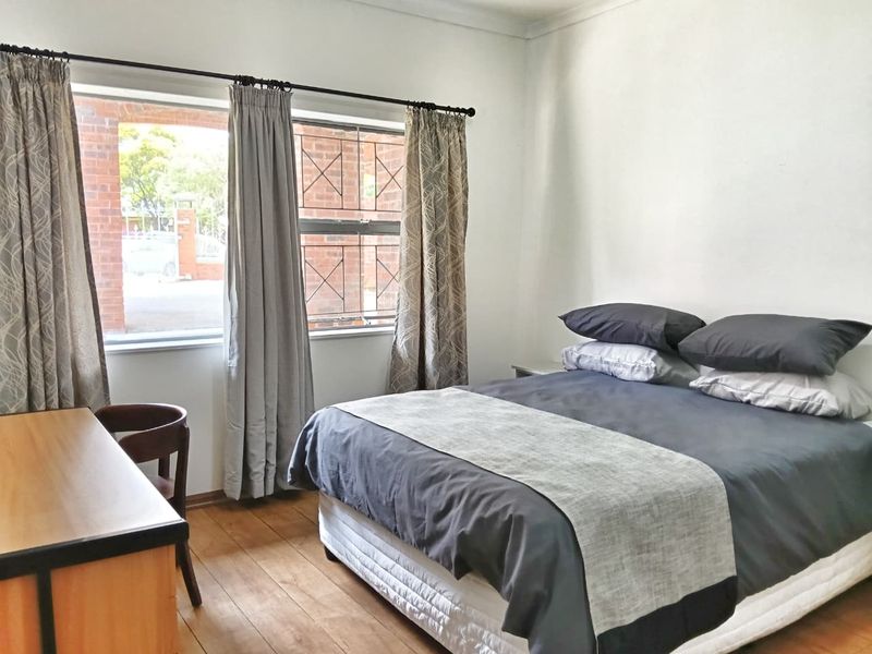 A bedroom featuring wooden flooring and a window with security bars, providing a functional and well-lit living space.