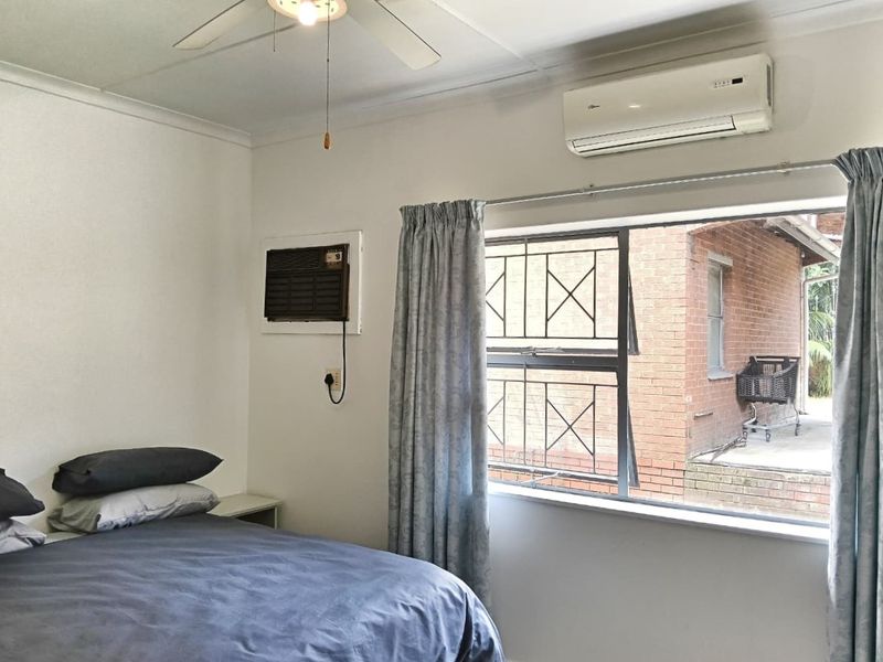 A bedroom featuring a ceiling fan, split-system air conditioning, and security bars on the window.