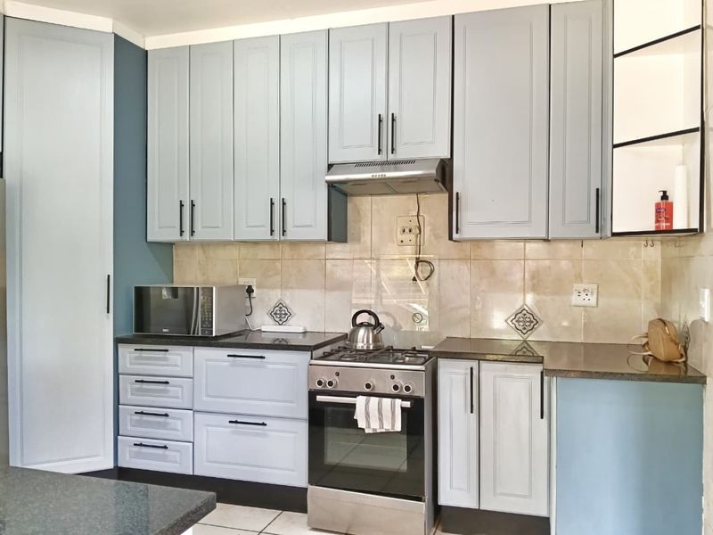A well-maintained kitchen featuring light blue cabinetry, stone countertops, a gas stove with extractor fan, and a tiled backsplash.