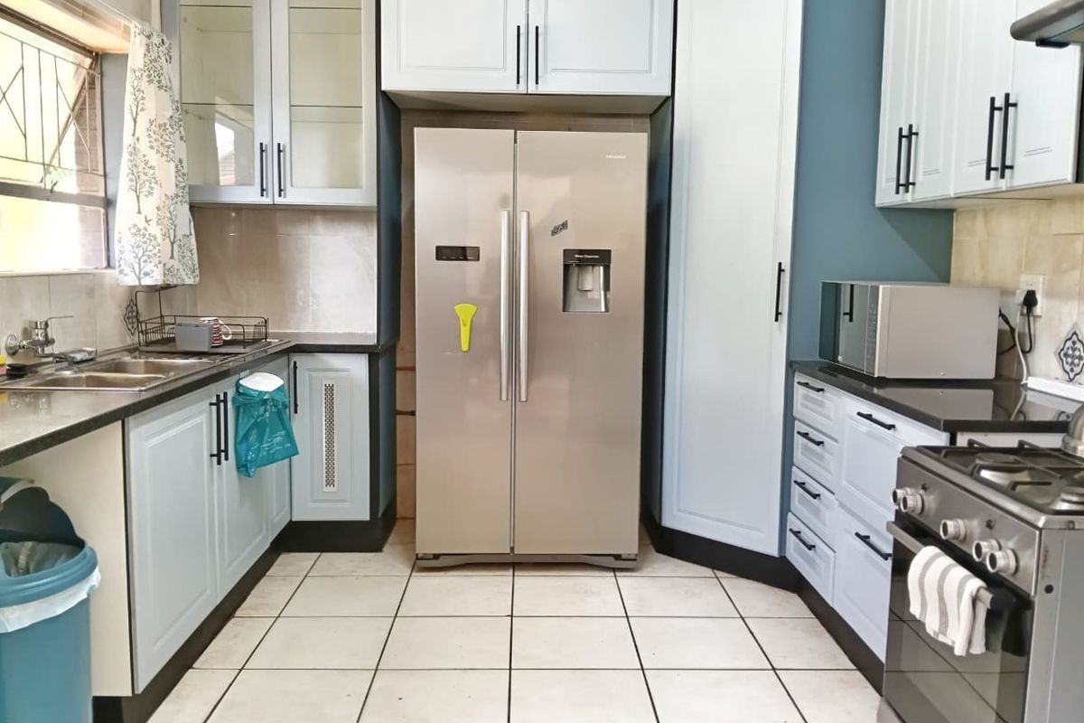 A functional kitchen featuring light blue cabinetry, dark countertops, tiled flooring, and a built-in gas stove with an extractor fan.
