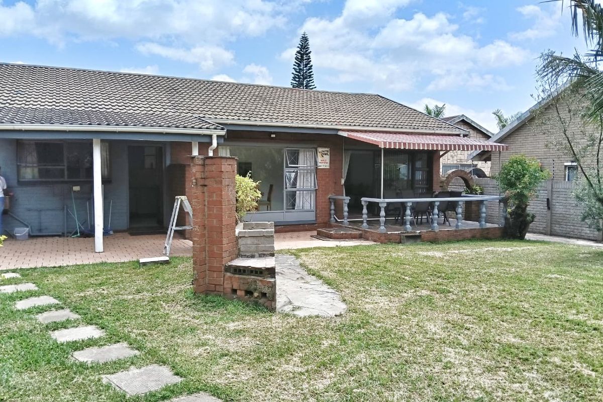 Rear view of the house featuring a covered patio with a balustrade, retractable awning, and a spacious garden area with paved pathways.