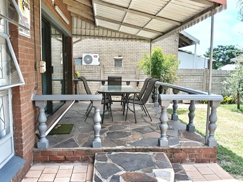 A covered patio area featuring stone paving, a brick facade, and a balustrade, providing a functional outdoor space for relaxation.