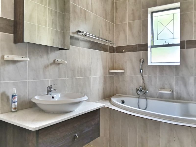 A clean, tiled bathroom featuring a modern vessel sink on a vanity cabinet, a built-in bathtub with a handheld shower mixer, and a medicine cabinet.