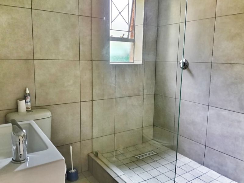 A clean, modern bathroom featuring a walk-in shower with a glass screen, tiled walls, and a functional basin and toilet setup.