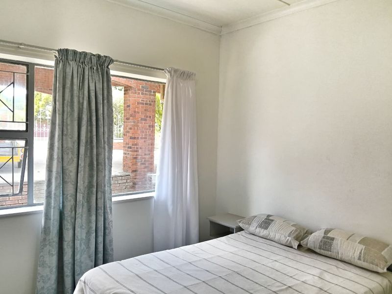 A simple bedroom featuring a window with security bars, providing natural light and a view of the exterior brick structure.