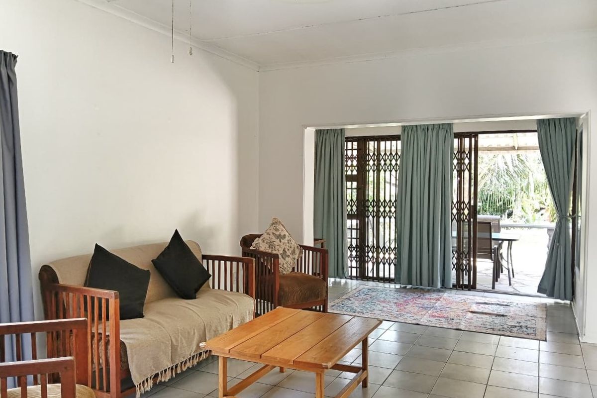 A spacious living room featuring tiled flooring, a ceiling fan, and large sliding glass doors that provide direct access to the outdoor patio area.