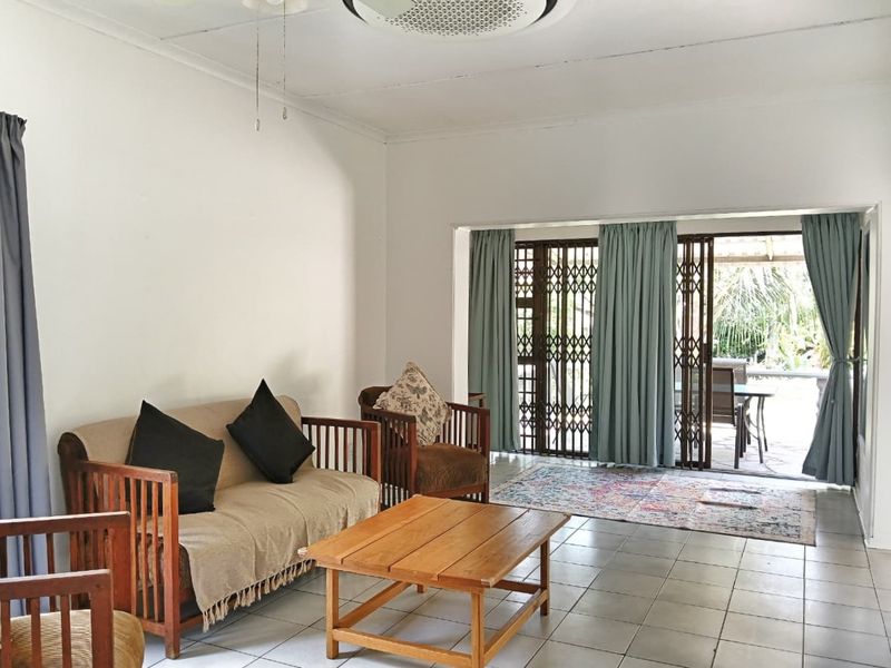 A spacious living room featuring tiled flooring, a ceiling fan, and large sliding glass doors that provide direct access to the outdoor patio area.
