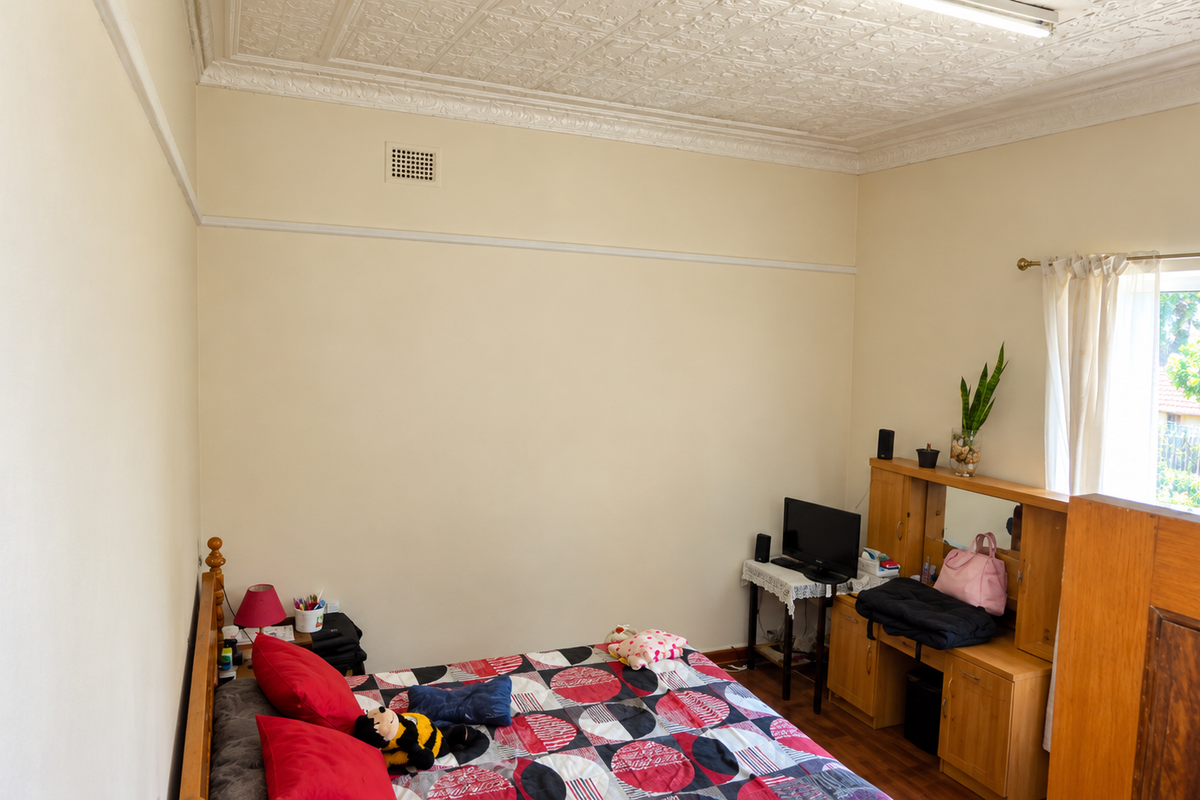 A bedroom featuring decorative ceiling tiles, picture rails, and timber flooring, offering a classic architectural character with natural light.