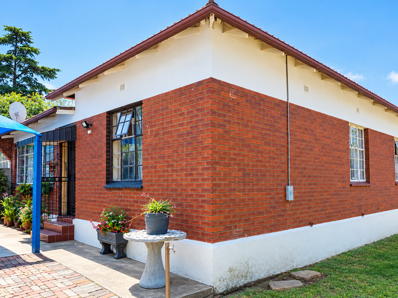 A well-maintained single-story brick house featuring a tiled roof, paved driveway, and secure entrance area with casement windows.