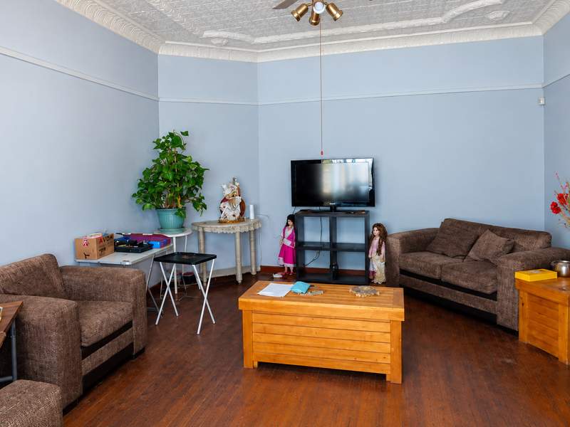 A living room featuring original pressed metal ceilings, hardwood flooring, and a picture rail, offering a classic architectural foundation for modern updates.