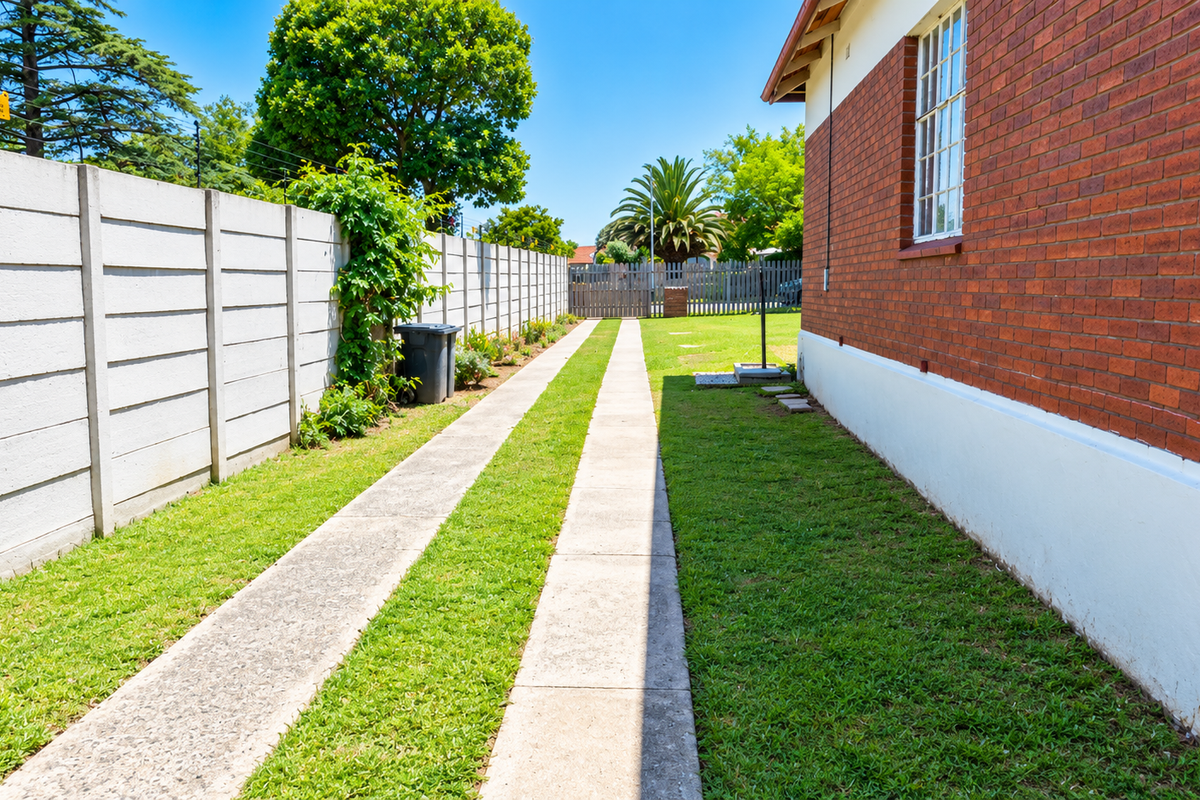 A side view of the property featuring a brick exterior wall, concrete driveway strips, and a precast concrete boundary wall enclosing the garden area.