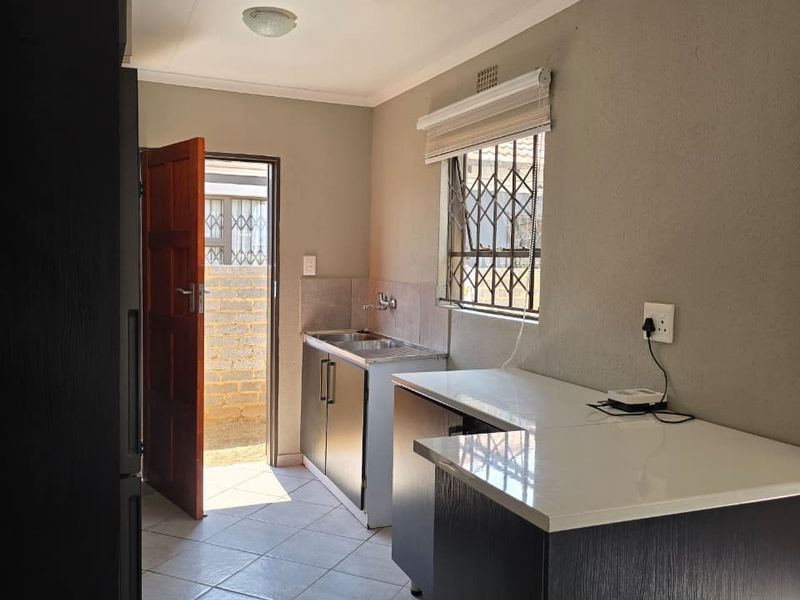 A functional kitchen featuring dark built-in cabinetry, light countertops, tiled flooring, and direct access to the exterior through a wooden door.