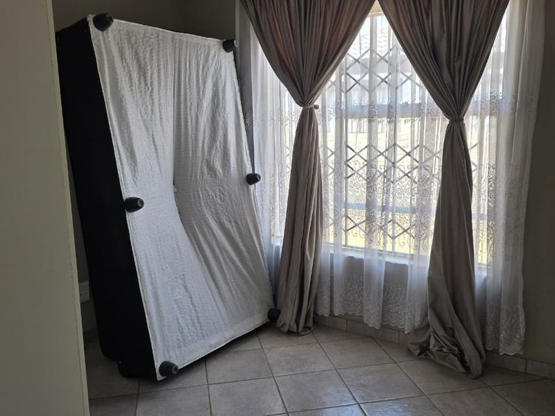 A bedroom featuring tiled flooring, security gate on the window, and neutral wall finishes.
