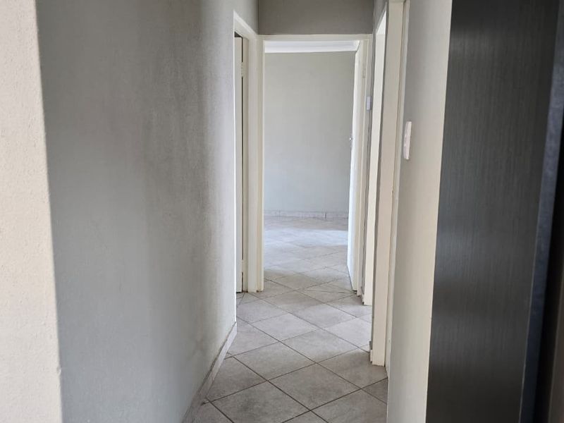A clean, empty hallway featuring neutral tiled flooring and a ceiling access hatch, providing access to multiple rooms within the home.