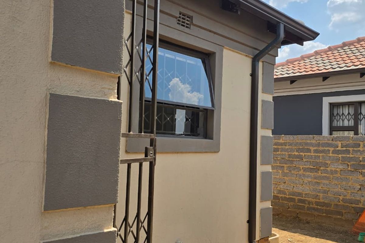 Rear exterior view of the property featuring a security gate, window with burglar bars, and functional downpipe drainage system.