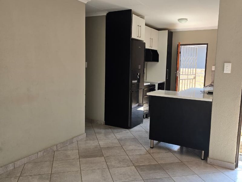 Open plan kitchen and living area featuring tiled flooring, modern cabinetry, and direct access to an outdoor area through a security gate.