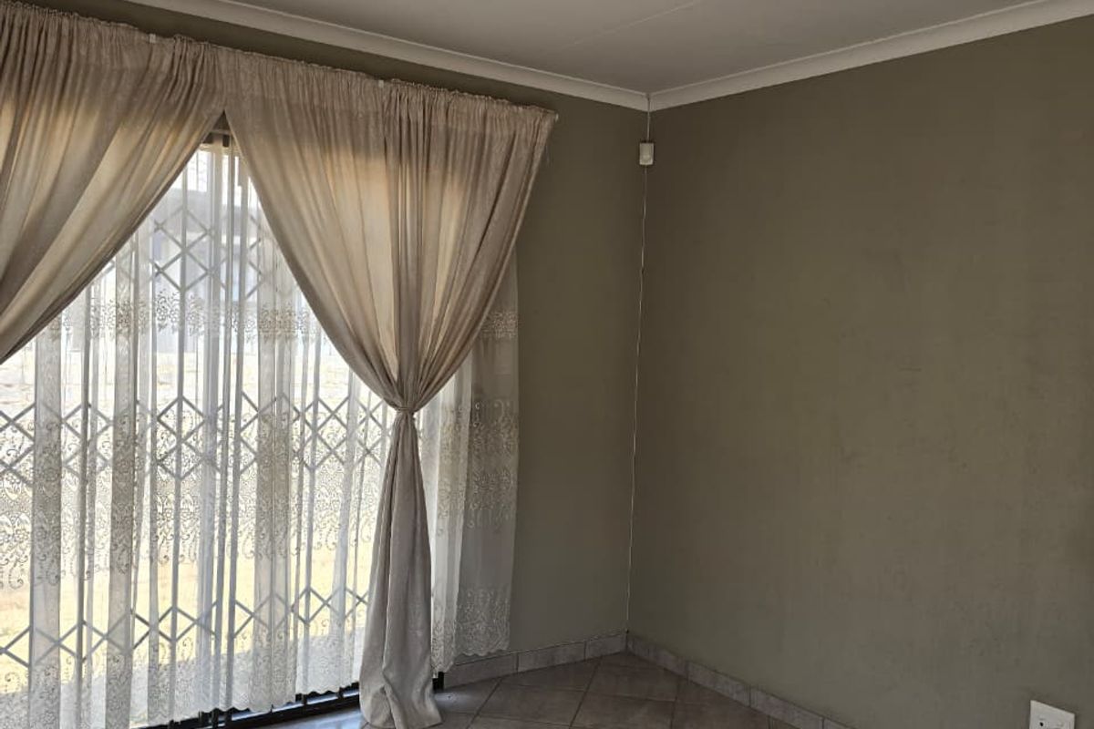 A vacant living area featuring neutral tiled flooring, a sliding door with a security gate, and plain walls, offering a blank canvas for interior design.