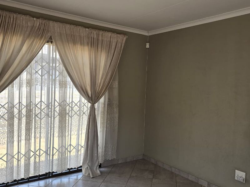 A vacant living area featuring neutral tiled flooring, a sliding door with a security gate, and plain walls, offering a blank canvas for interior design.