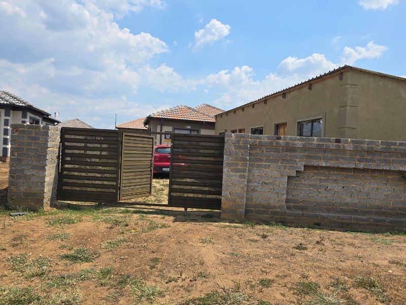 Front view of the property featuring a brick boundary wall and metal driveway gate, with an unfinished exterior wall finish.
