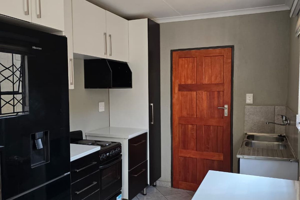 A functional kitchen featuring white and black cabinetry, a double stainless steel sink, tiled flooring, and a solid wood door leading to the exterior.