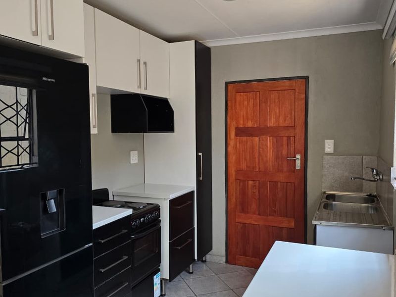 A functional kitchen featuring white and black cabinetry, a double stainless steel sink, tiled flooring, and a solid wood door leading to the exterior.