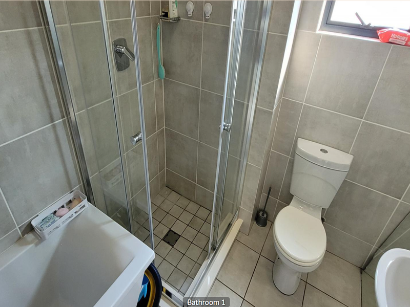 A functional bathroom featuring a glass shower enclosure, a standard toilet, and neutral wall and floor tiling.