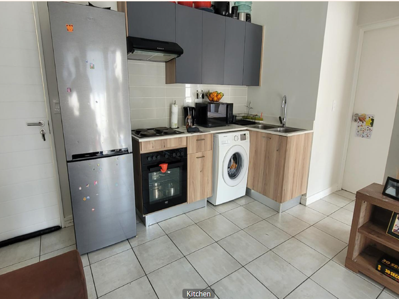 Compact kitchen featuring modern wood-finish cabinetry, built-in oven, hob, extractor fan, and integrated laundry appliance space with tiled flooring.