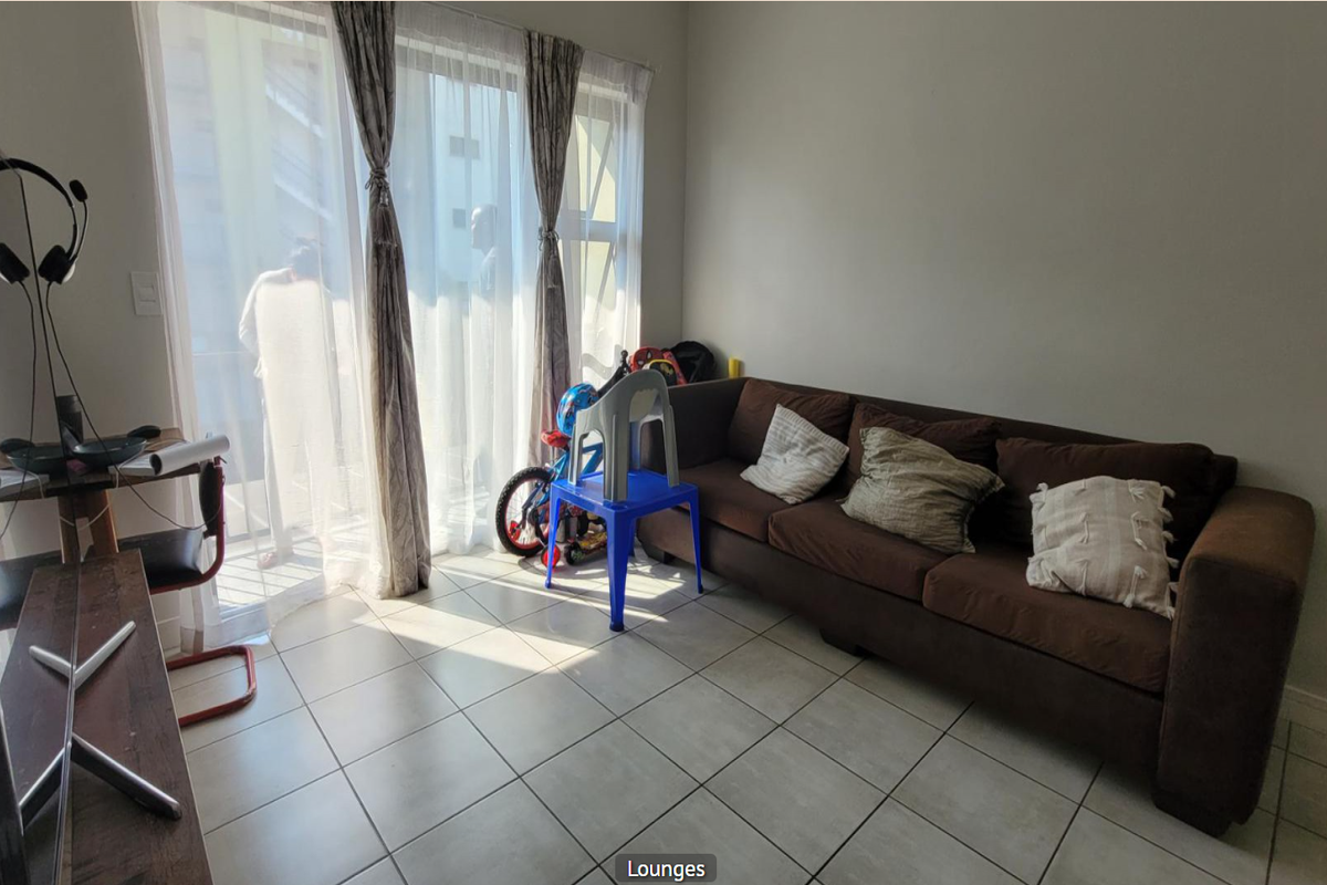 A living room area featuring tiled flooring and a large sliding glass door that provides access to the balcony and natural light.