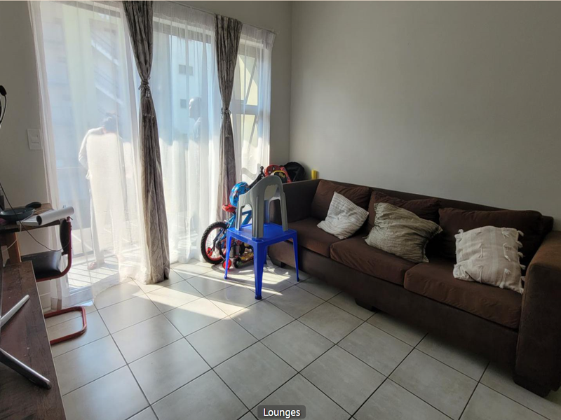 A living room area featuring tiled flooring and a large sliding glass door that provides access to the balcony and natural light.