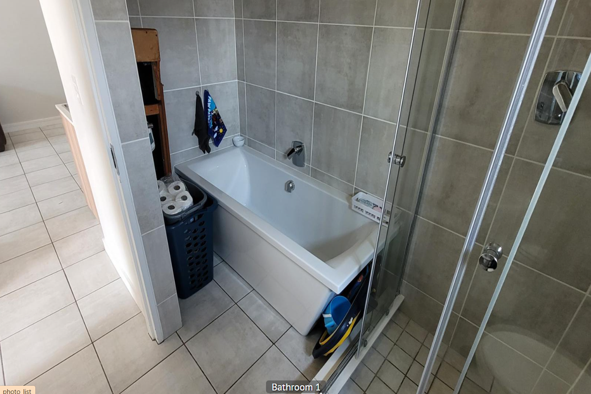A functional bathroom featuring a built-in bathtub, a glass-enclosed shower, and neutral ceramic tiling throughout.