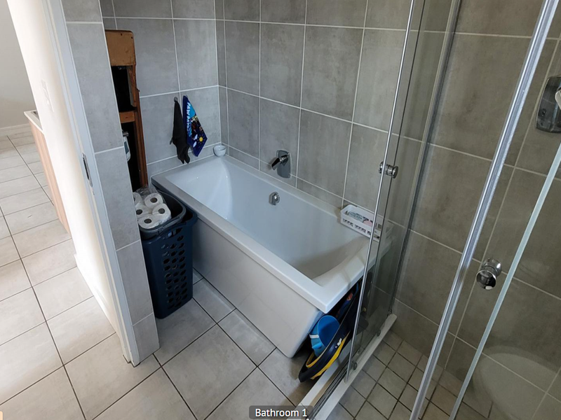 A functional bathroom featuring a built-in bathtub, a glass-enclosed shower, and neutral ceramic tiling throughout.