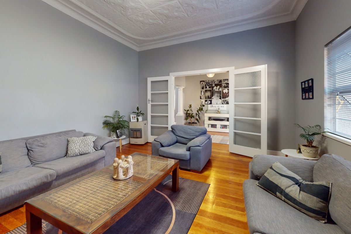 Spacious living room featuring polished hardwood timber floors, an ornate pressed metal ceiling, and classic french doors leading to an adjoining space.