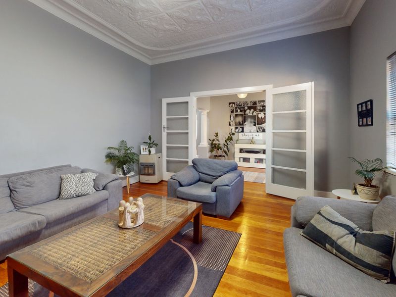 Spacious living room featuring polished hardwood timber floors, an ornate pressed metal ceiling, and classic french doors leading to an adjoining space.