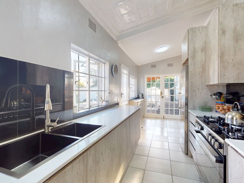 Modern kitchen featuring sleek cabinetry, gas hob, oven, double sink, tiled flooring, and elegant pressed metal ceilings with direct access to the patio.