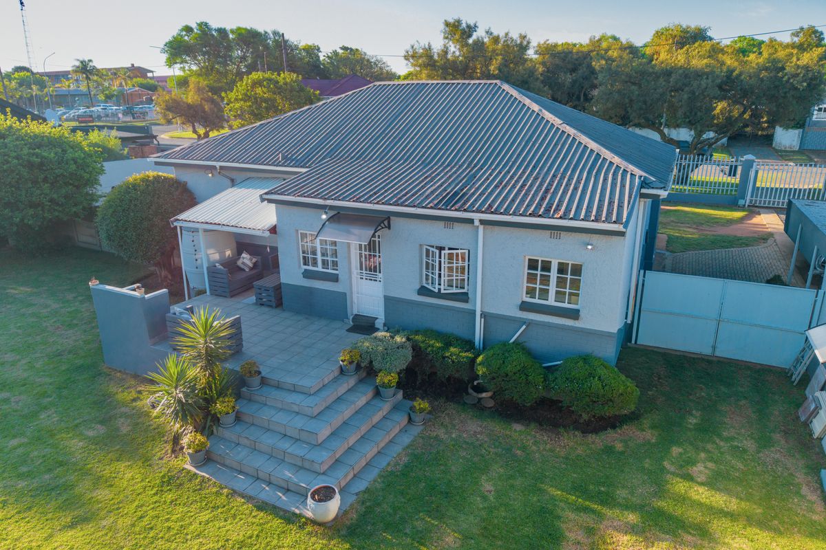 Aerial view of the rear exterior featuring a tiled patio, concrete stairs, and a well-maintained garden area with metal roof structure.