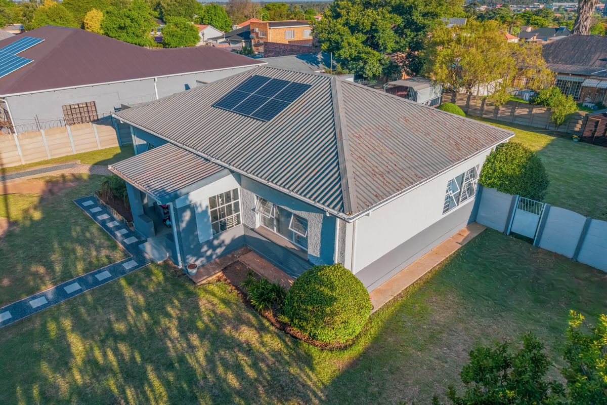 Aerial view of a residential property featuring a corrugated metal roof with installed solar panels, surrounded by a garden and perimeter boundary walls.