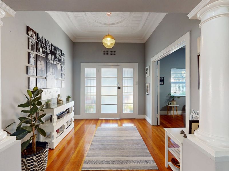 Welcoming entrance hall featuring polished hardwood flooring, ornate columns, and a decorative ceiling rose, leading into the main living areas of the home.